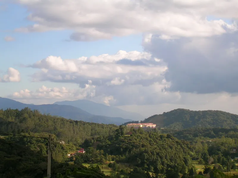 Forested hills with a large hotel building on a ridge, mountains and clouds behind